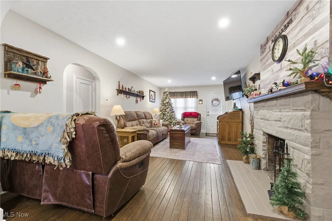 Living area featuring dark wood-type flooring, a stone fireplace, arched walkways, and recessed lighting