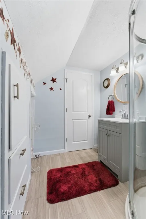 Bathroom with vanity, a textured ceiling, lofted ceiling, a stall shower, and light wood-style floors