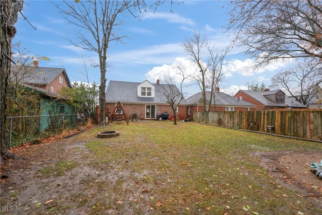 Rear view of property with a fenced backyard, a fire pit, brick siding, and a chimney
