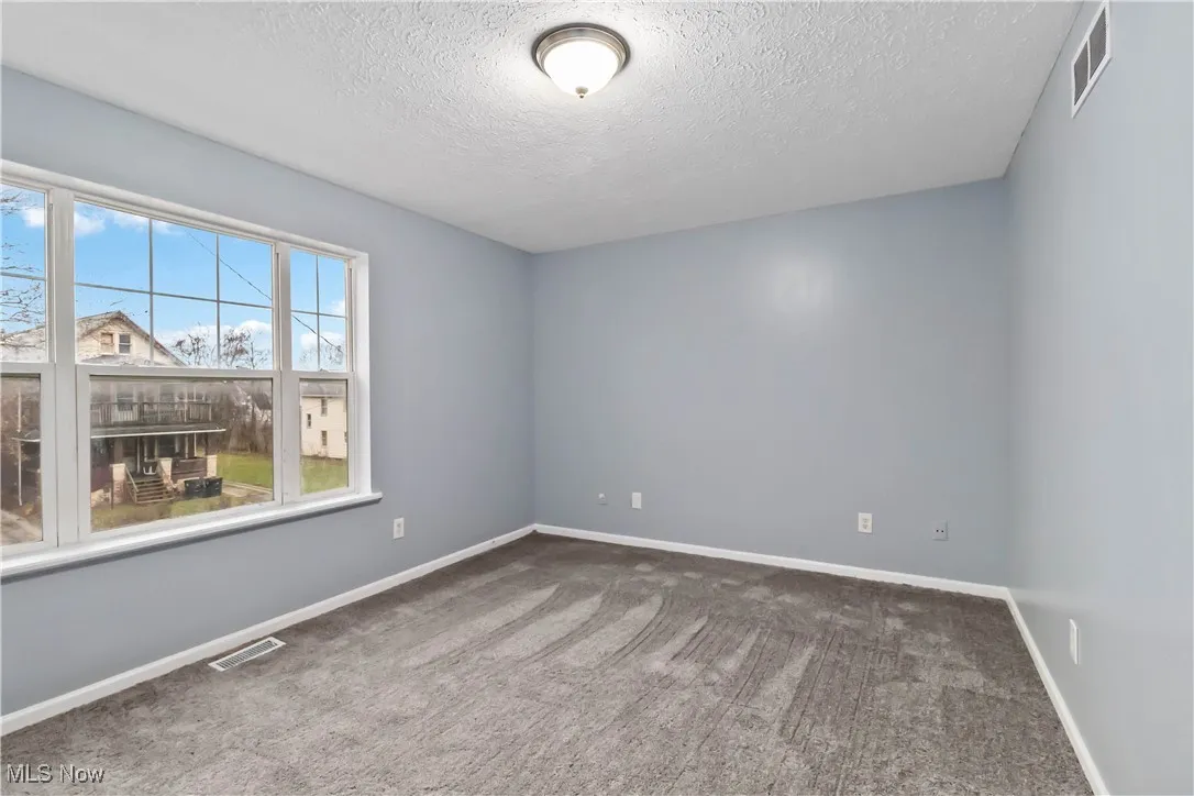 Carpeted empty room with a textured ceiling and baseboards