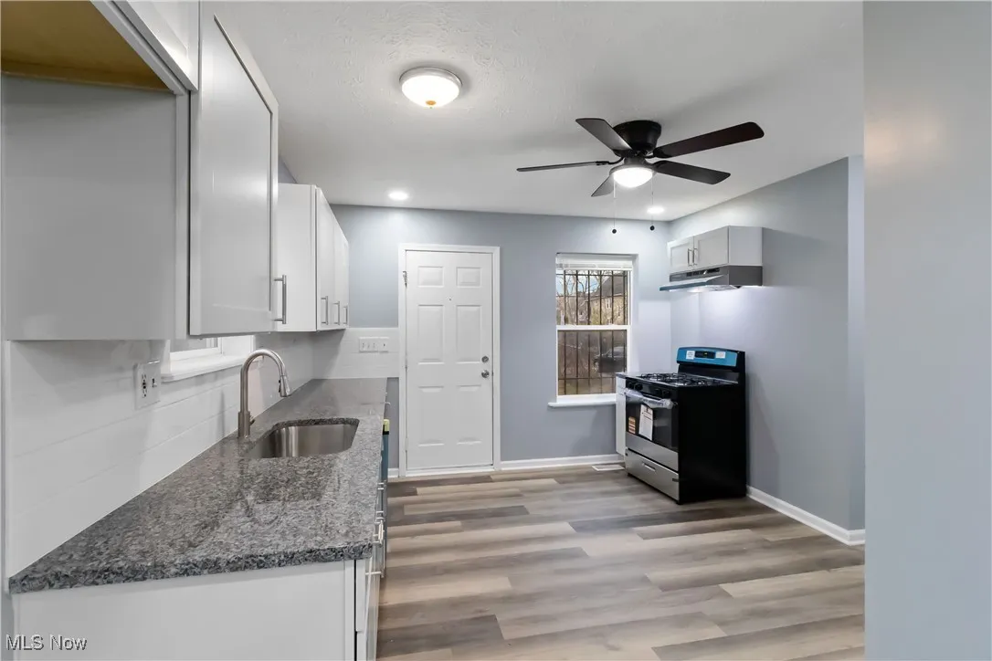 Kitchen featuring dark stone countertops, gas stove, dark wood-style flooring, ceiling fan, and white cabinetry