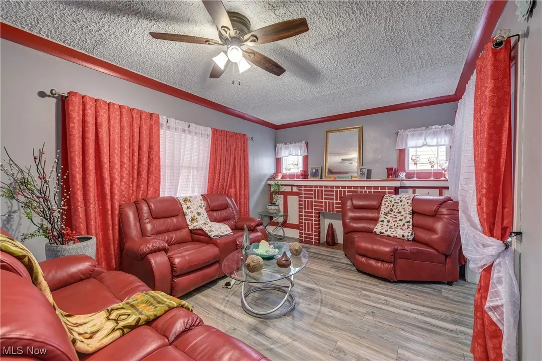 Living room featuring wood finished floors, a textured ceiling, ornamental molding, and ceiling fan