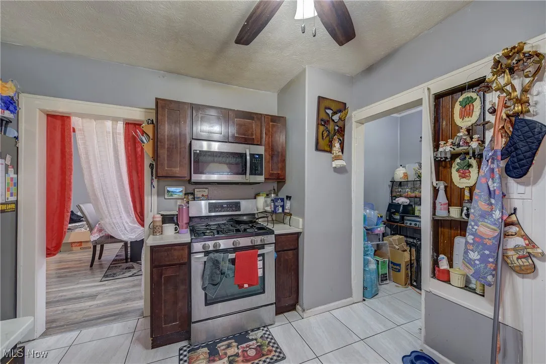 Kitchen featuring appliances with stainless steel finishes, a textured ceiling, light countertops, dark brown cabinetry, and light tile patterned flooring