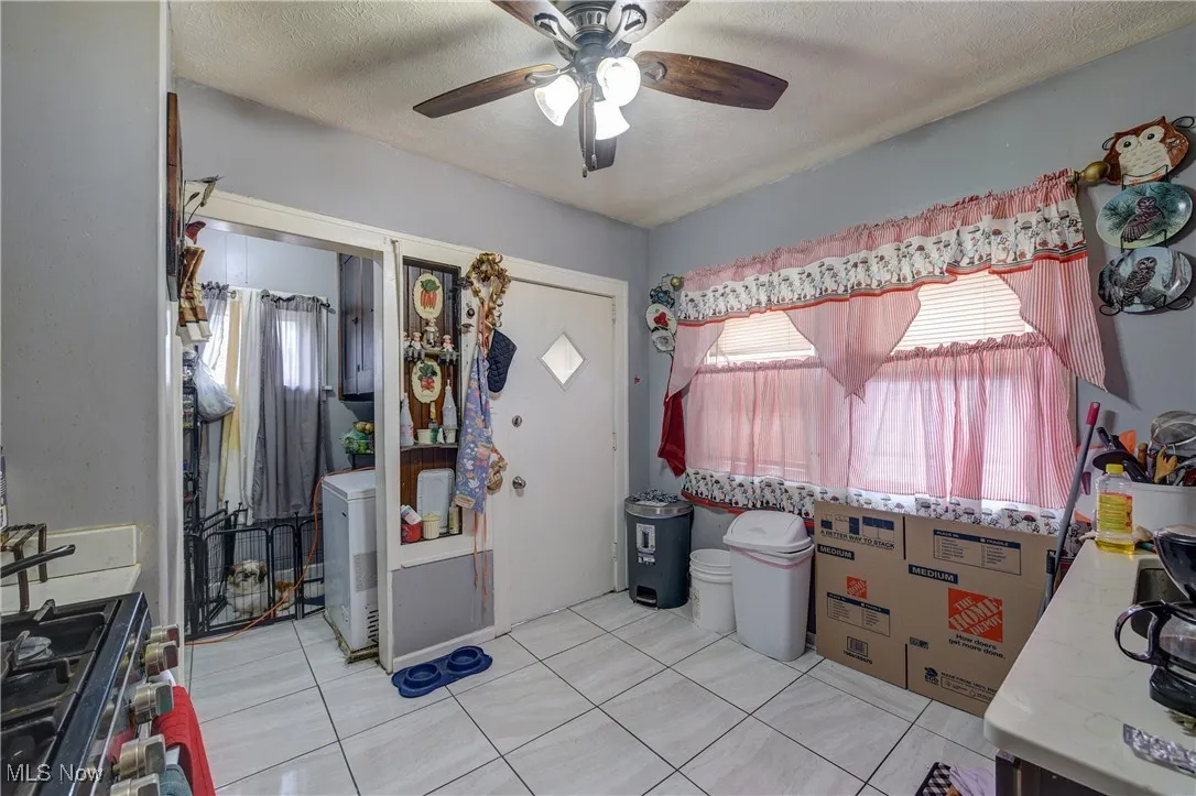 Kitchen featuring gas stove, light tile patterned flooring, a textured ceiling, ceiling fan, and light countertops
