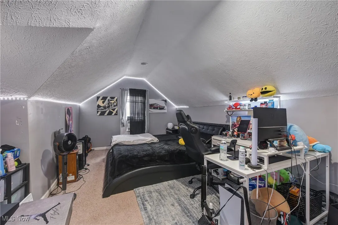 Bedroom featuring a textured ceiling, vaulted ceiling, carpet, and a desk