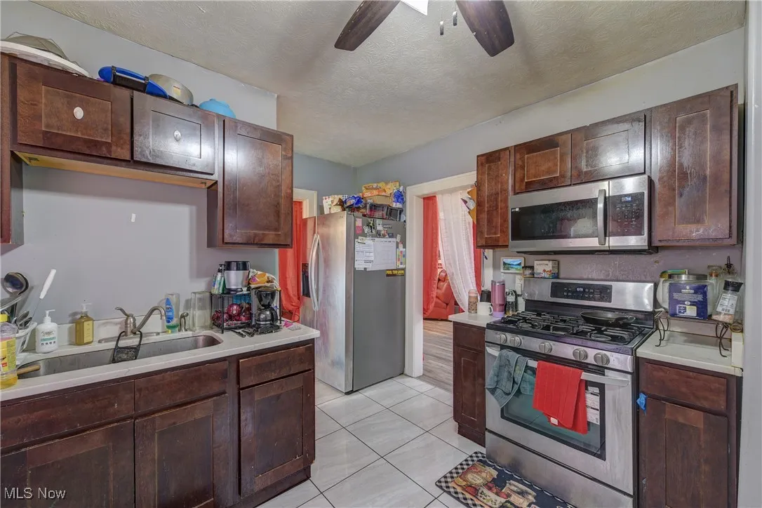 Kitchen featuring appliances with stainless steel finishes, light countertops, a textured ceiling, and dark brown cabinets