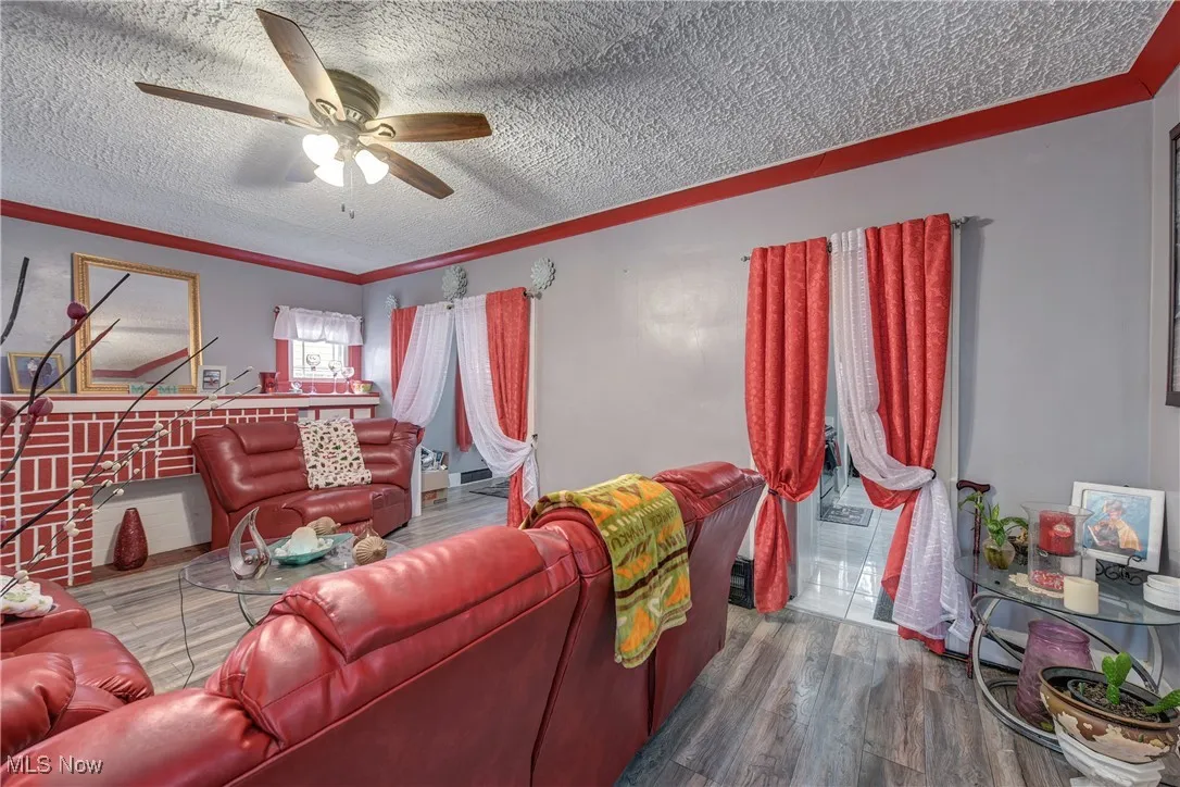 Living area with wood finished floors, a ceiling fan, a textured ceiling, and ornamental molding