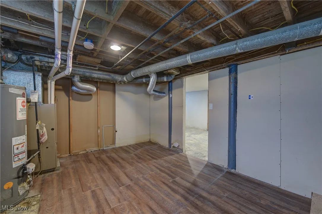 Unfinished basement with gas water heater and dark wood-type flooring