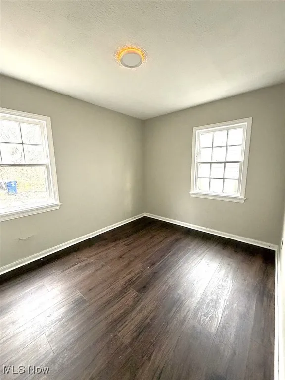 Empty room with plenty of natural light, a textured ceiling, and dark wood-style flooring