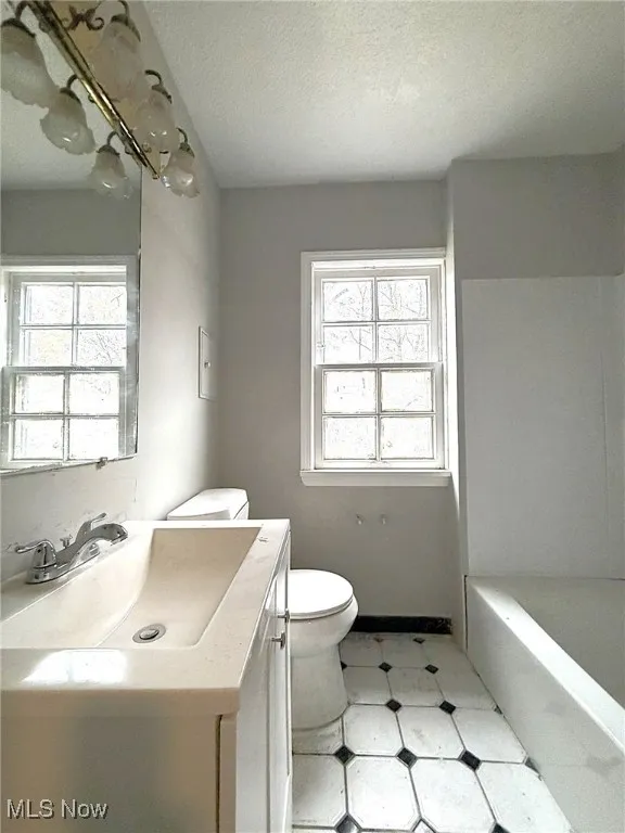 Bathroom with vanity, a textured ceiling, light floors, and healthy amount of natural light