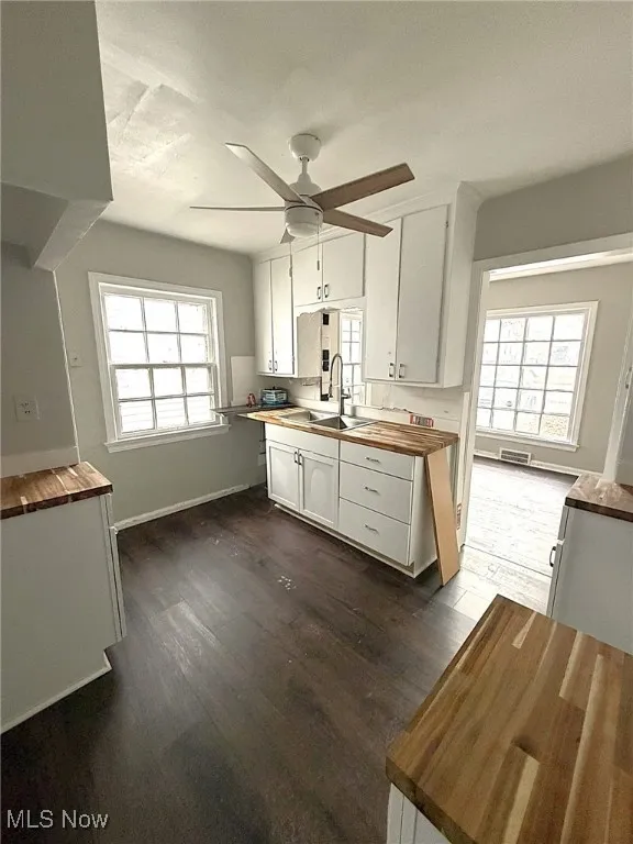 Kitchen with butcher block countertops, white cabinets, ceiling fan, and dark wood-style flooring