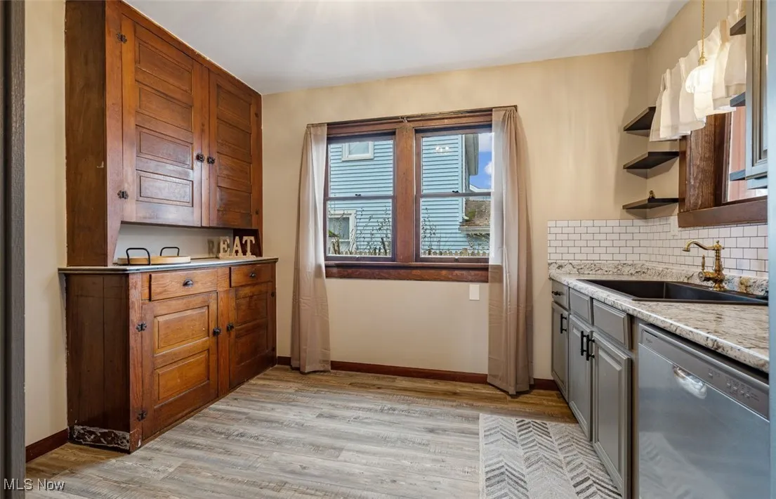 Kitchen featuring stainless steel dishwasher, tasteful backsplash, light wood finished floors, and open shelves