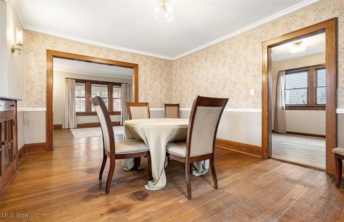 Dining space with wallpapered walls, light wood-style flooring, and a wainscoted wall