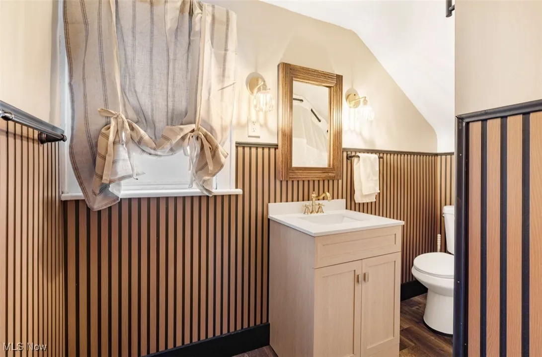 Half bathroom with lofted ceiling, vanity, dark wood-type flooring, and a wainscoted wall