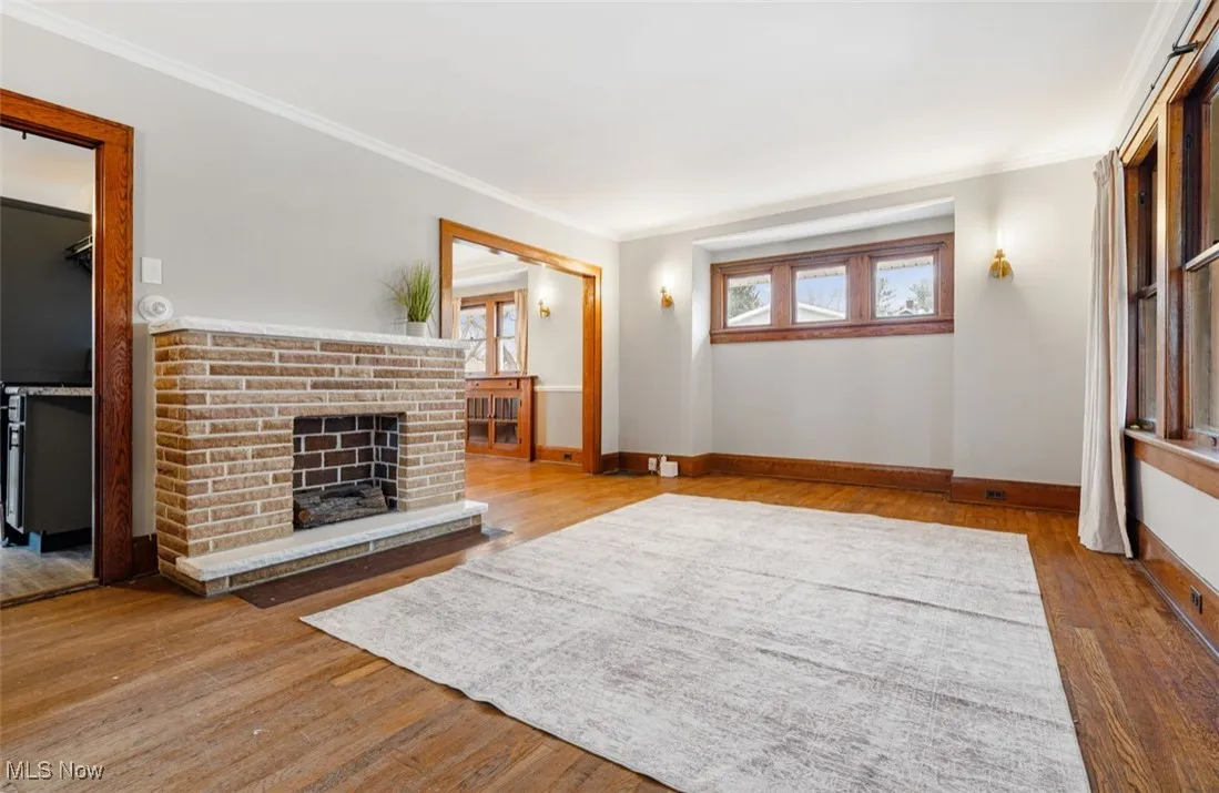 Unfurnished living room featuring light wood finished floors, a fireplace, healthy amount of natural light, and crown molding