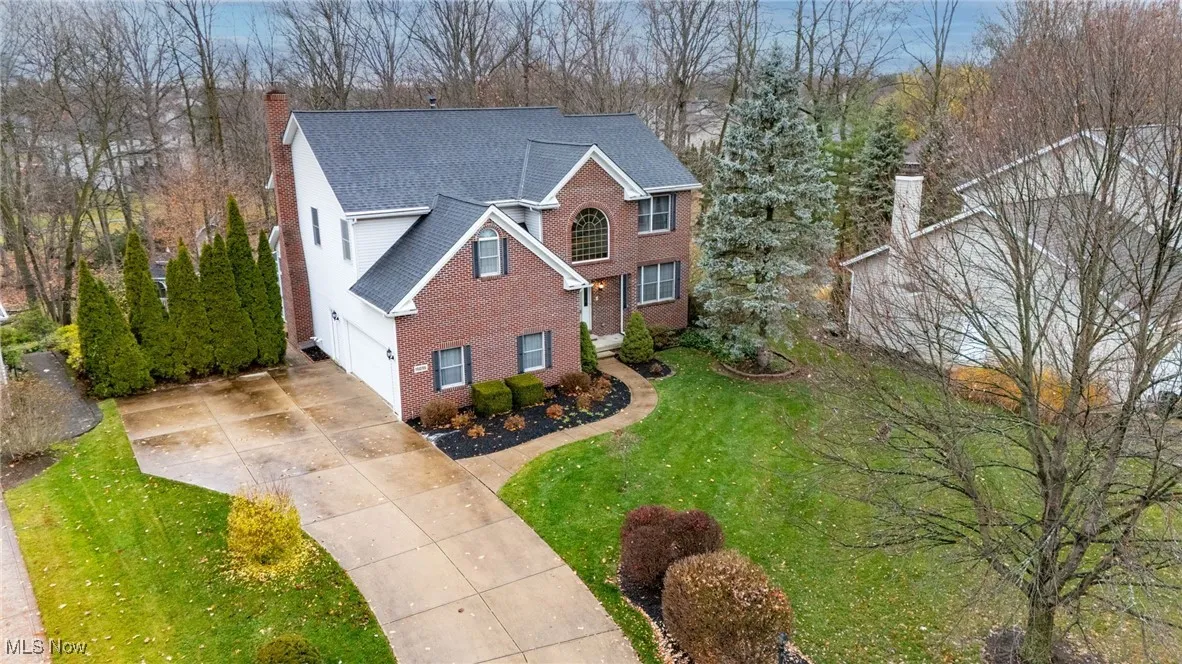 View of front of property featuring a chimney, brick siding, concrete driveway, a front yard, and roof with shingles
