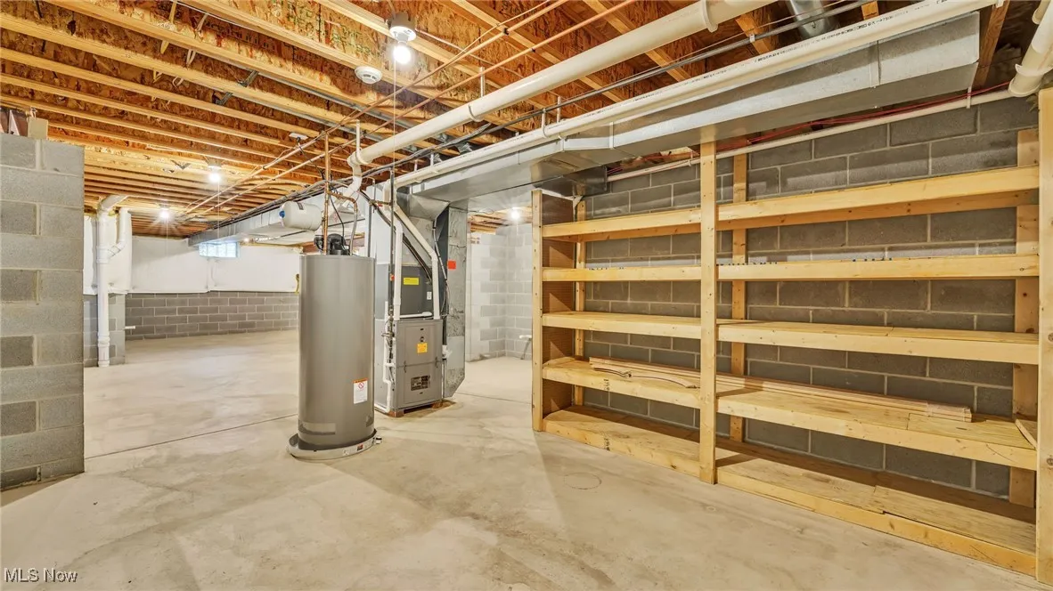 Unfinished basement area featuring storage shelves, water heater and heating unit