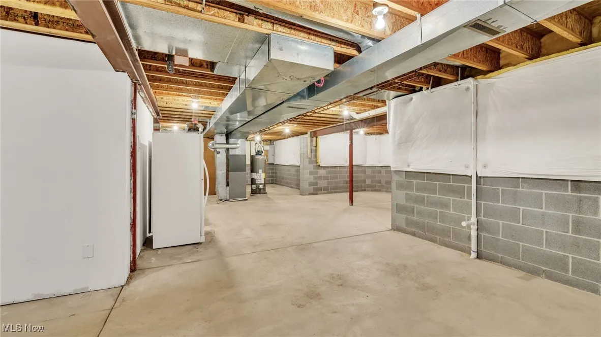 Unfinished basement with freestanding refrigerator, heating unit, and gas water heater