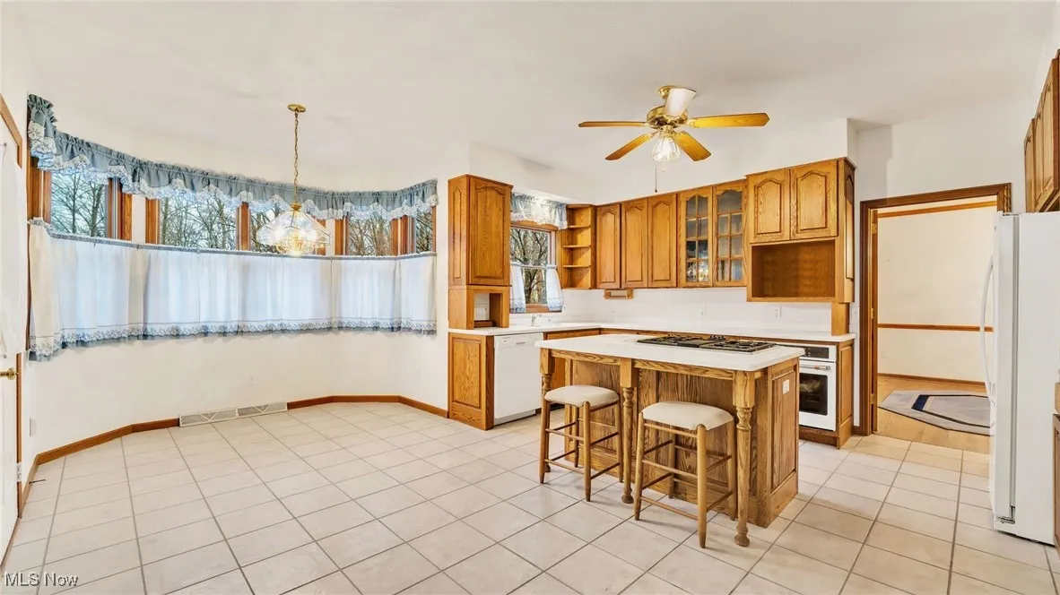 Kitchen featuring cabinets, light Corion countertops, island, white appliances, and glass insert cabinets