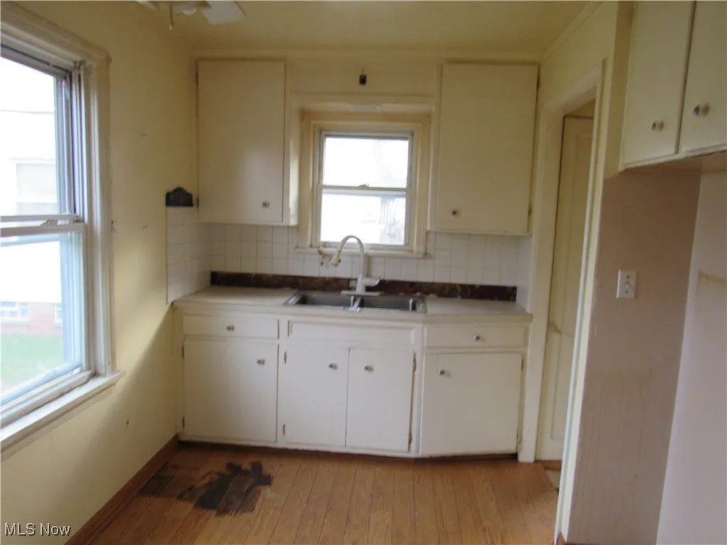 Kitchen with backsplash, light wood finished floors, light countertops, and white cabinets