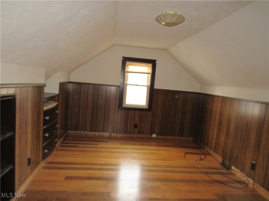 Bonus room with vaulted ceiling, wooden walls, dark wood-type flooring, a textured ceiling, and a wainscoted wall