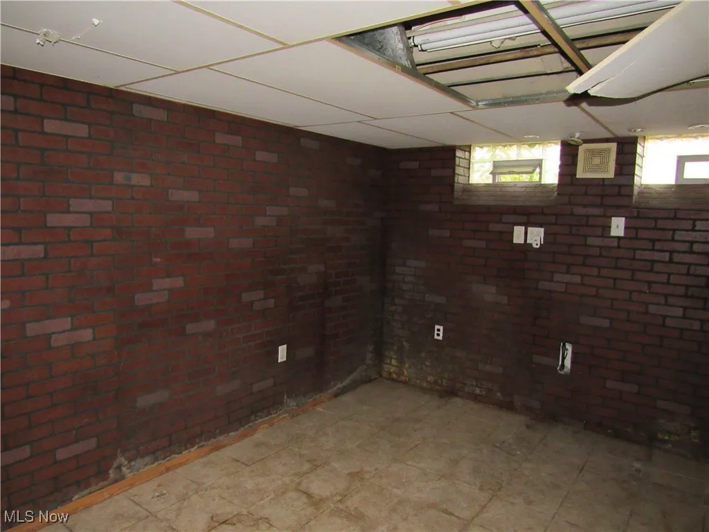 Basement featuring a paneled ceiling and brick wall