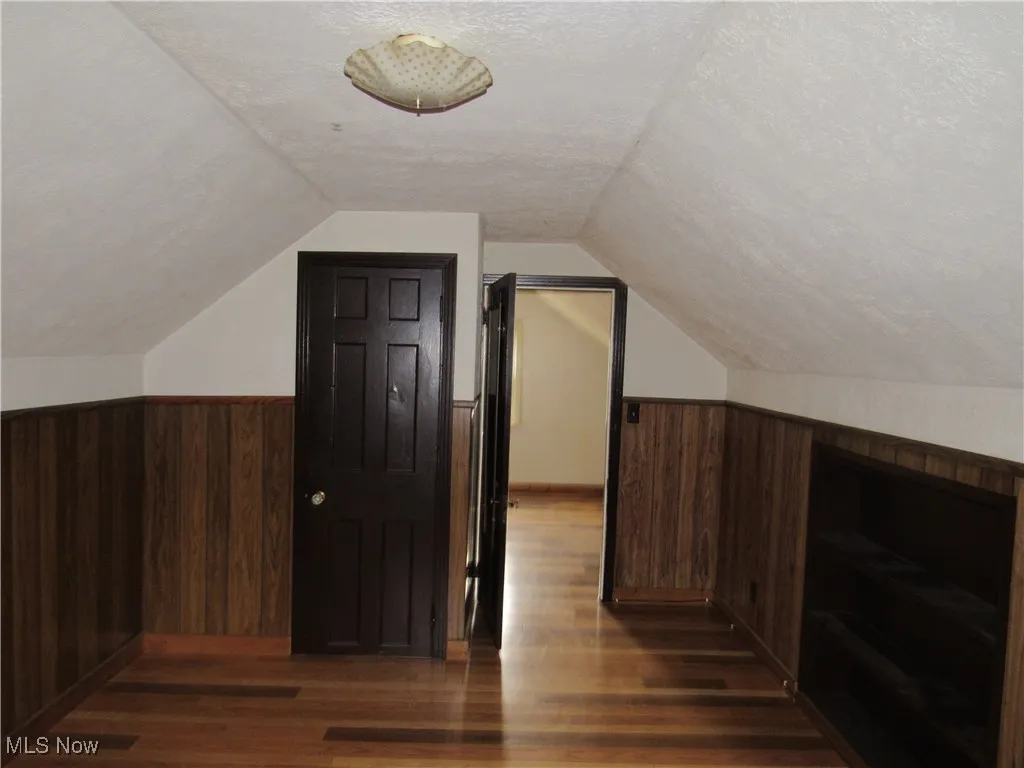 Additional living space with wooden walls, lofted ceiling, dark wood-type flooring, and a wainscoted wall