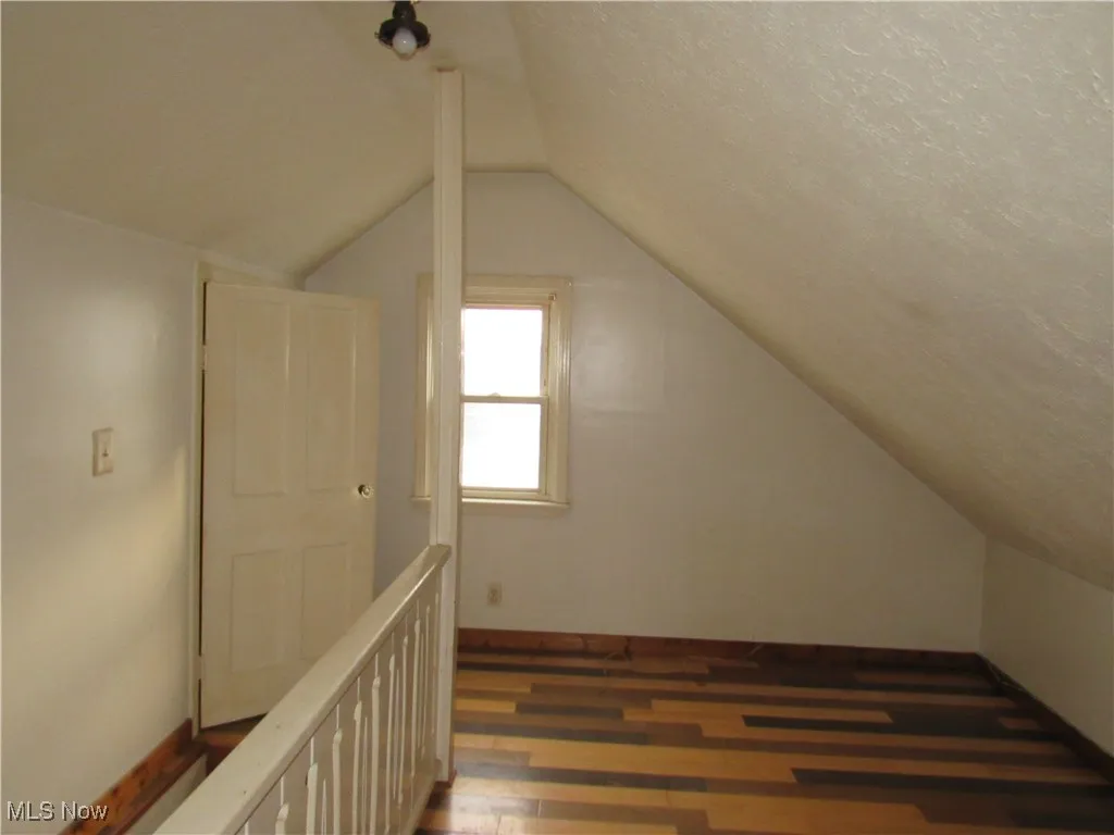 Additional living space with dark wood-style flooring, vaulted ceiling, and a textured ceiling