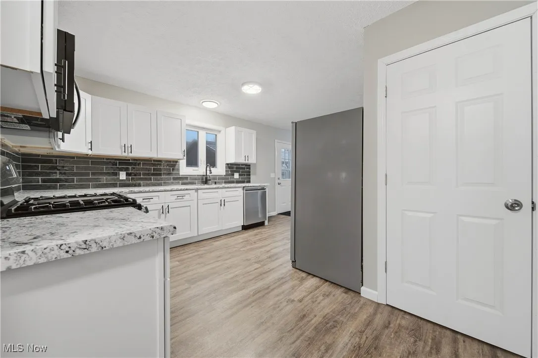 Kitchen with white cabinetry, black appliances, tasteful backsplash, light wood finished floors, and a textured ceiling
