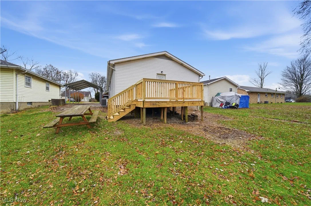 Rear view of house with a lawn, a wooden deck, a detached carport, and stairs