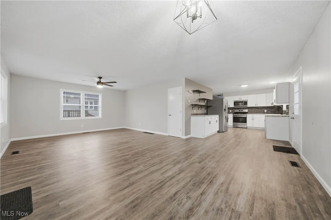 Unfurnished living room featuring healthy amount of natural light, light wood finished floors, ceiling fan, and a textured ceiling