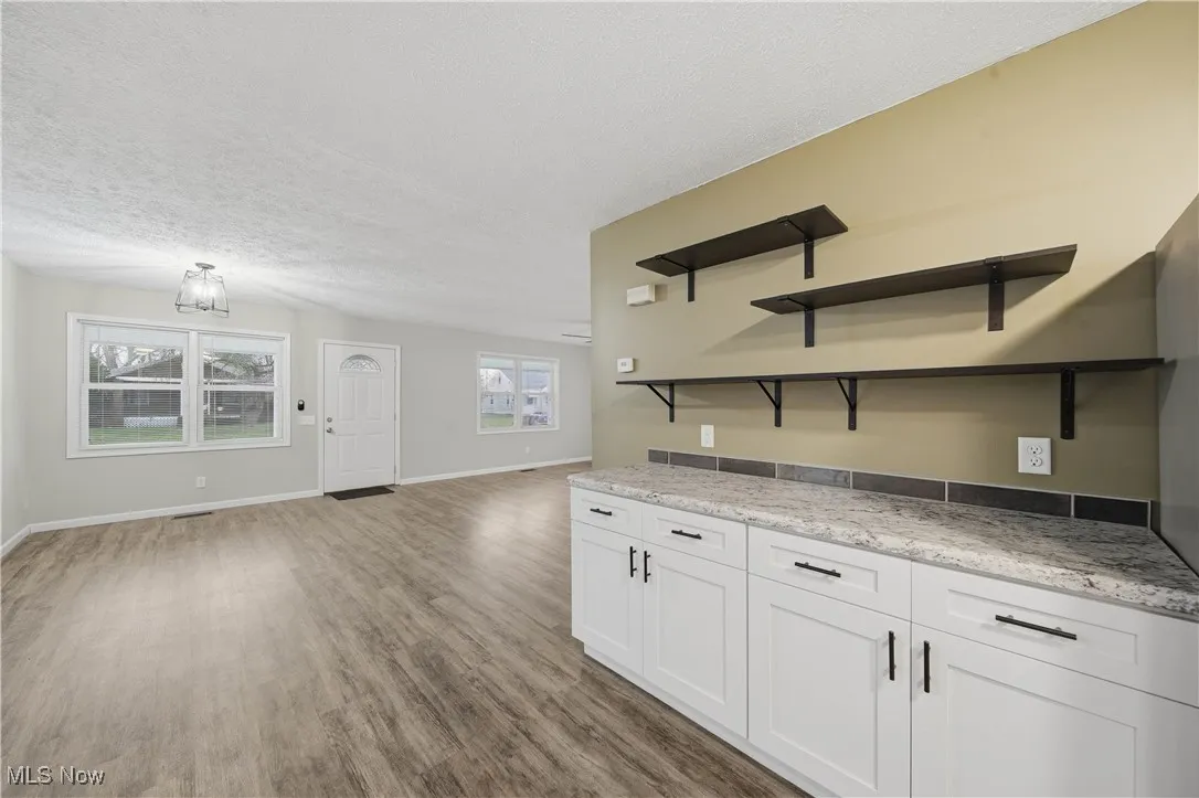 Kitchen featuring open shelves, white cabinetry, a textured ceiling, light wood finished floors, and light stone countertops