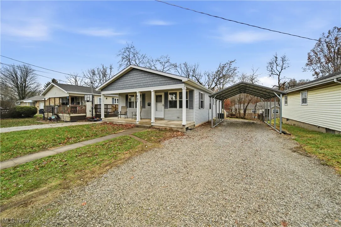 View of front of house with driveway, covered porch, a detached carport, and a front yard