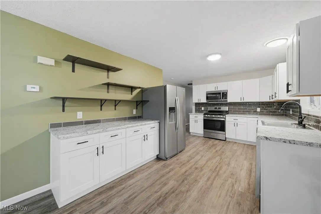 Kitchen with open shelves, white cabinetry, stainless steel appliances, and light wood-type flooring