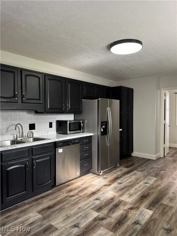 Kitchen with dark cabinetry, tasteful backsplash, stainless steel appliances, dark wood finished floors, and a textured ceiling