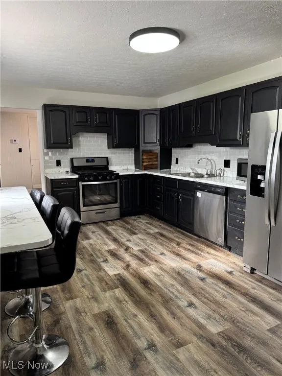 Kitchen featuring dark cabinetry, stainless steel appliances, dark wood-type flooring, a textured ceiling, and tasteful backsplash