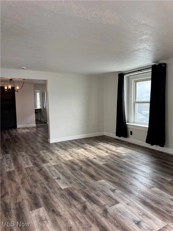 Spare room with a textured ceiling, dark wood-type flooring, and a chandelier
