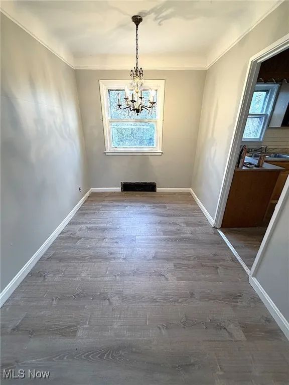 Unfurnished dining area with light wood-style floors, a chandelier, and ornamental molding