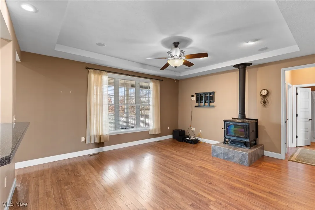 Unfurnished living room featuring a raised ceiling, a wood stove, and light wood-type flooring