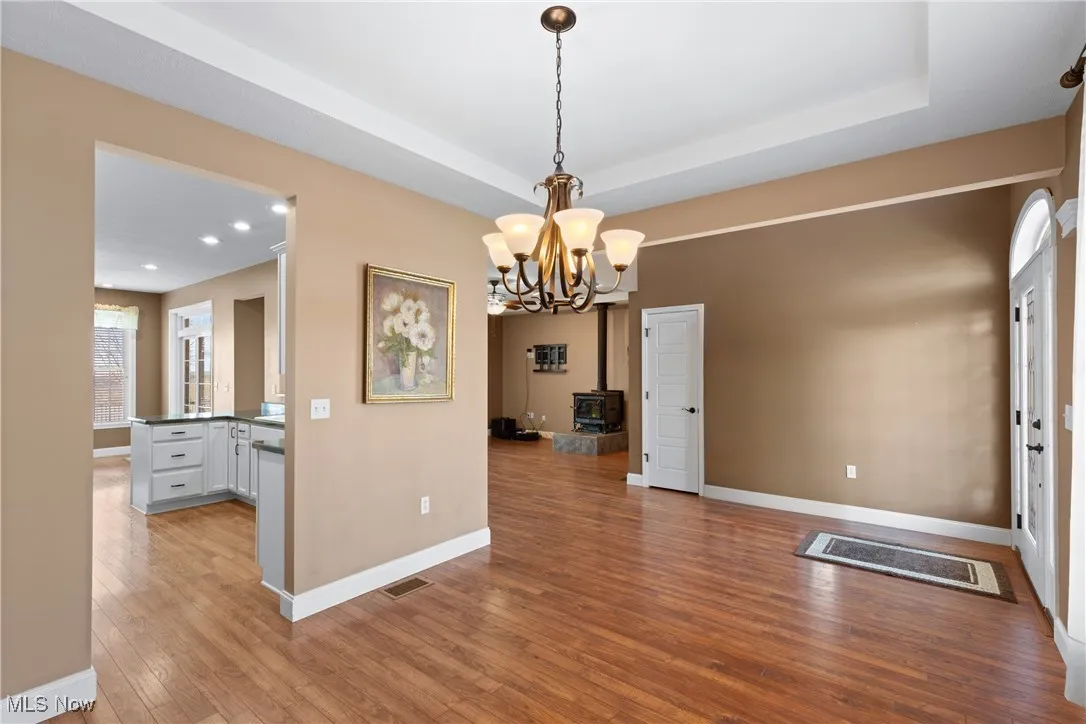 Unfurnished dining area featuring light wood-style floors, a wood stove, a tray ceiling, recessed lighting, and a chandelier