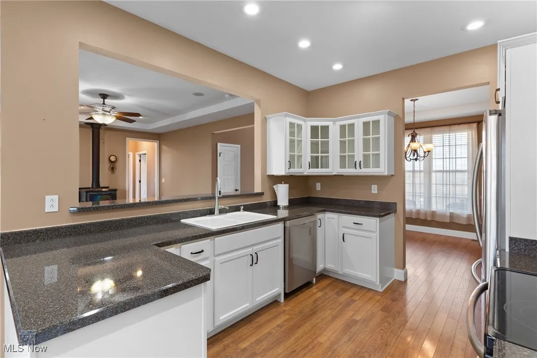 Kitchen featuring glass insert cabinets, white cabinets, appliances with stainless steel finishes, light wood finished floors, and a wood stove