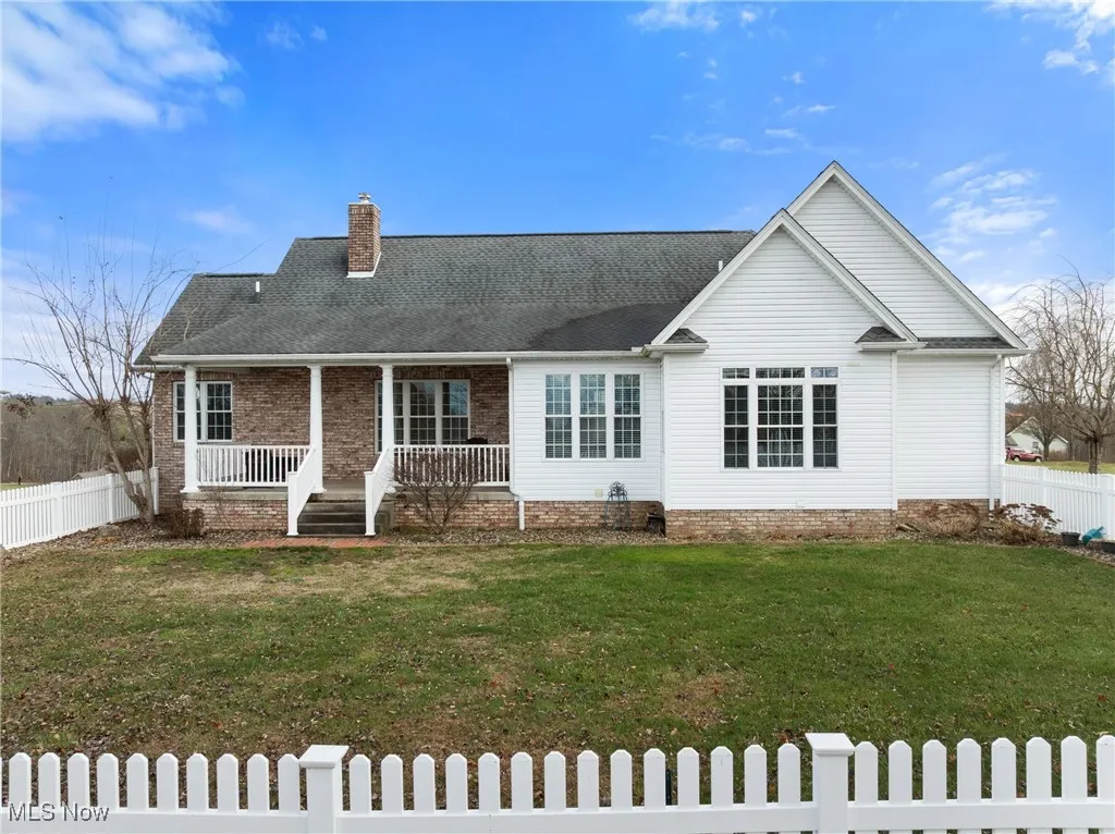 View of back of home featuring a porch, a shingled roof, and a chimney