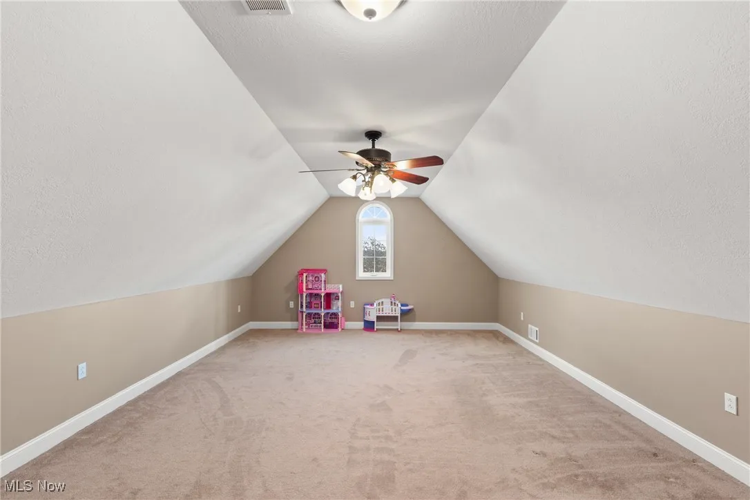 Additional living space with a textured ceiling, light carpet, vaulted ceiling, and a ceiling fan