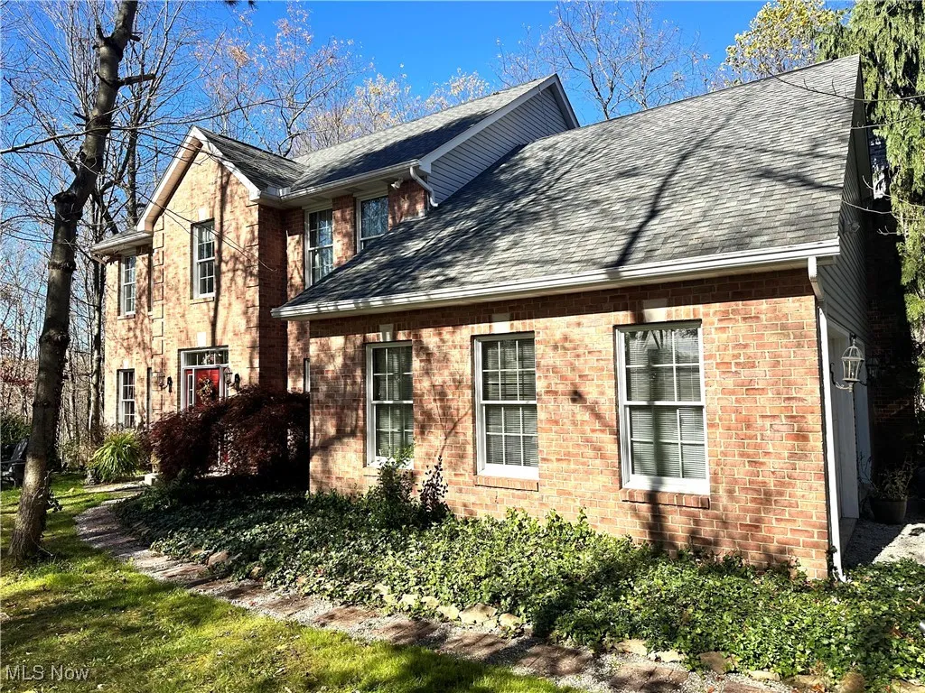 View of front of house featuring a shingled roof, brick siding, and a front yard
