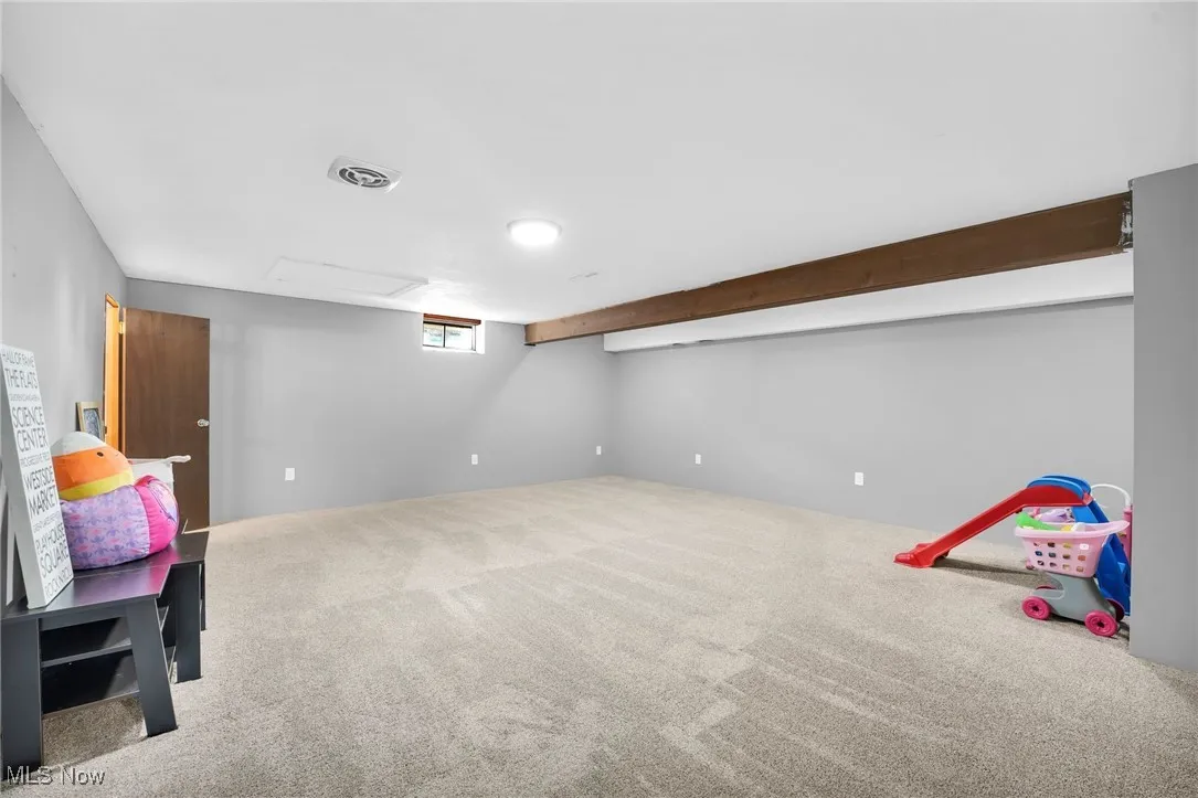 Another view of the finished basement with decorative wood beam, carpet and recessed lighting