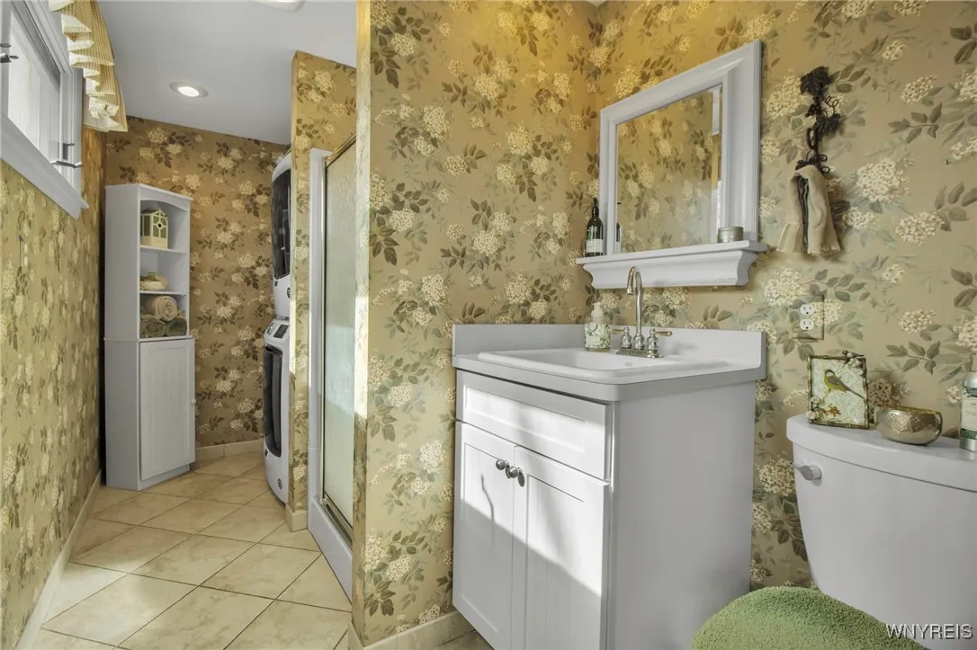 Bath/laundry has ceramic tiled flr, vanity/laundry tub + shower stall + stack washer+dryer