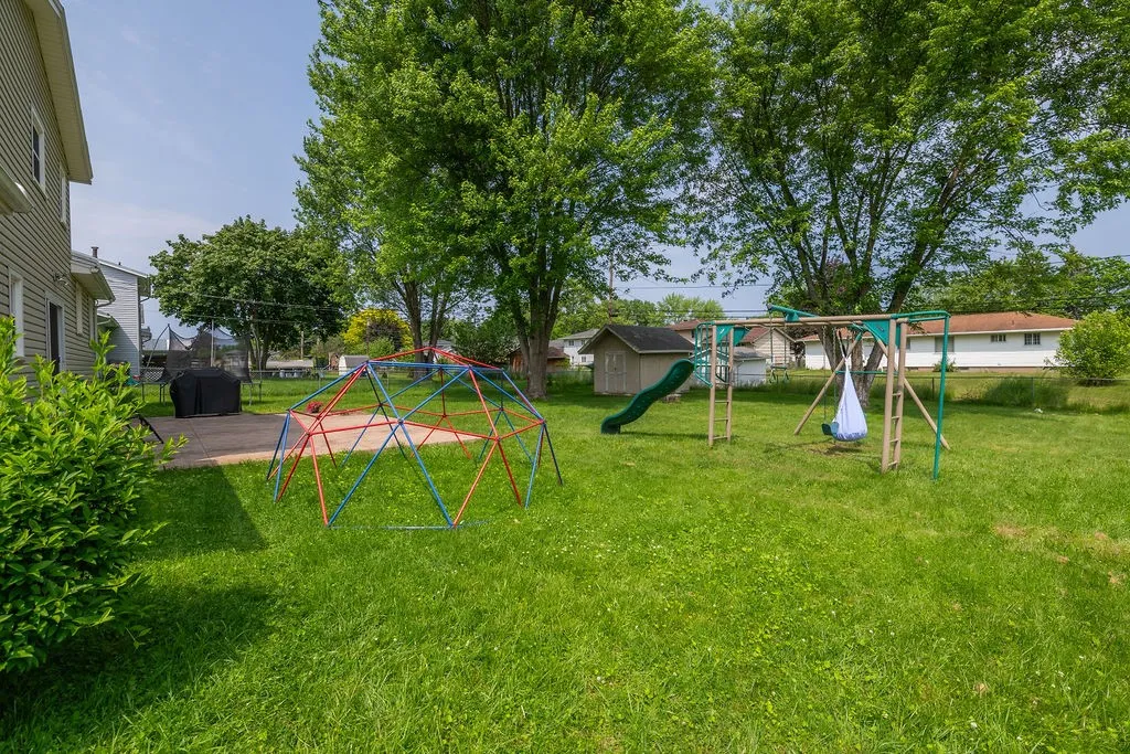 Backyard has playsets, a stamped concrete patio, firepit, shed and mature trees