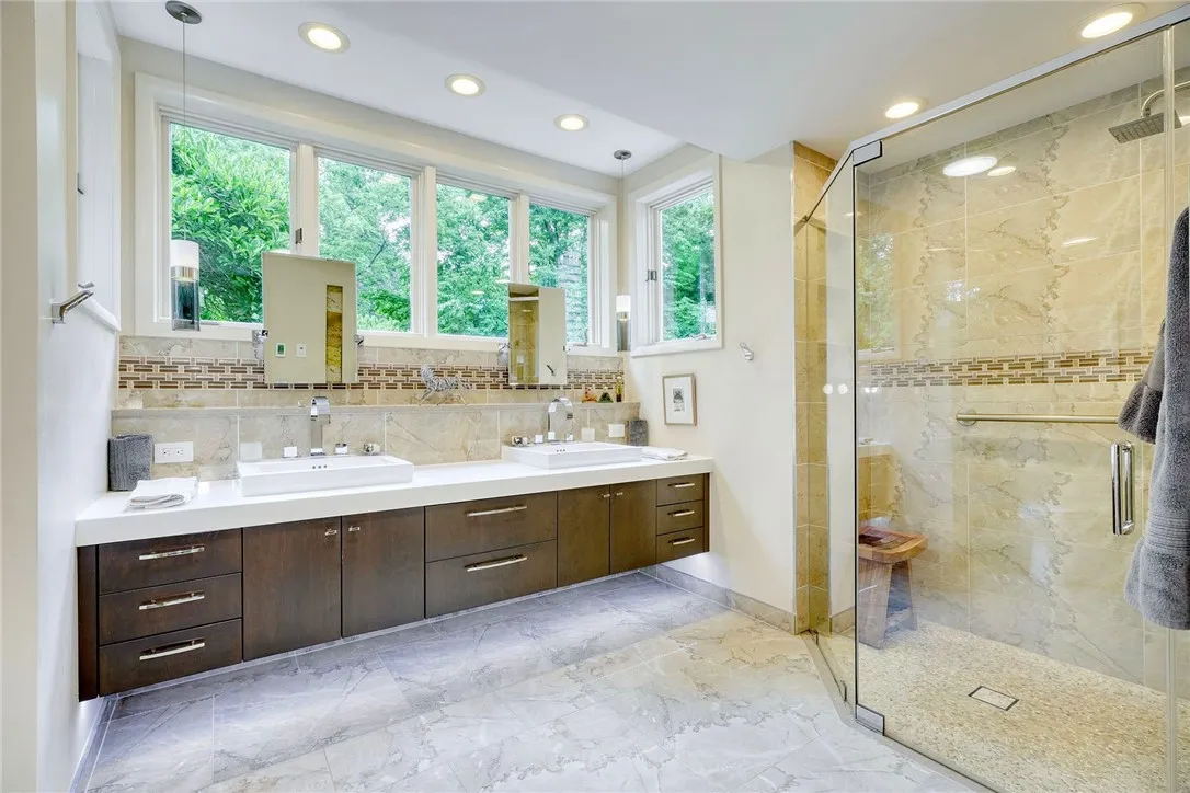 Remodeled Spa-Like en suite with heated porcelain tile, floating double vanity with underlighting, curbless shower, rainfall head + body jets. Windows wrap the vanity, bringing in natural light + treetop views