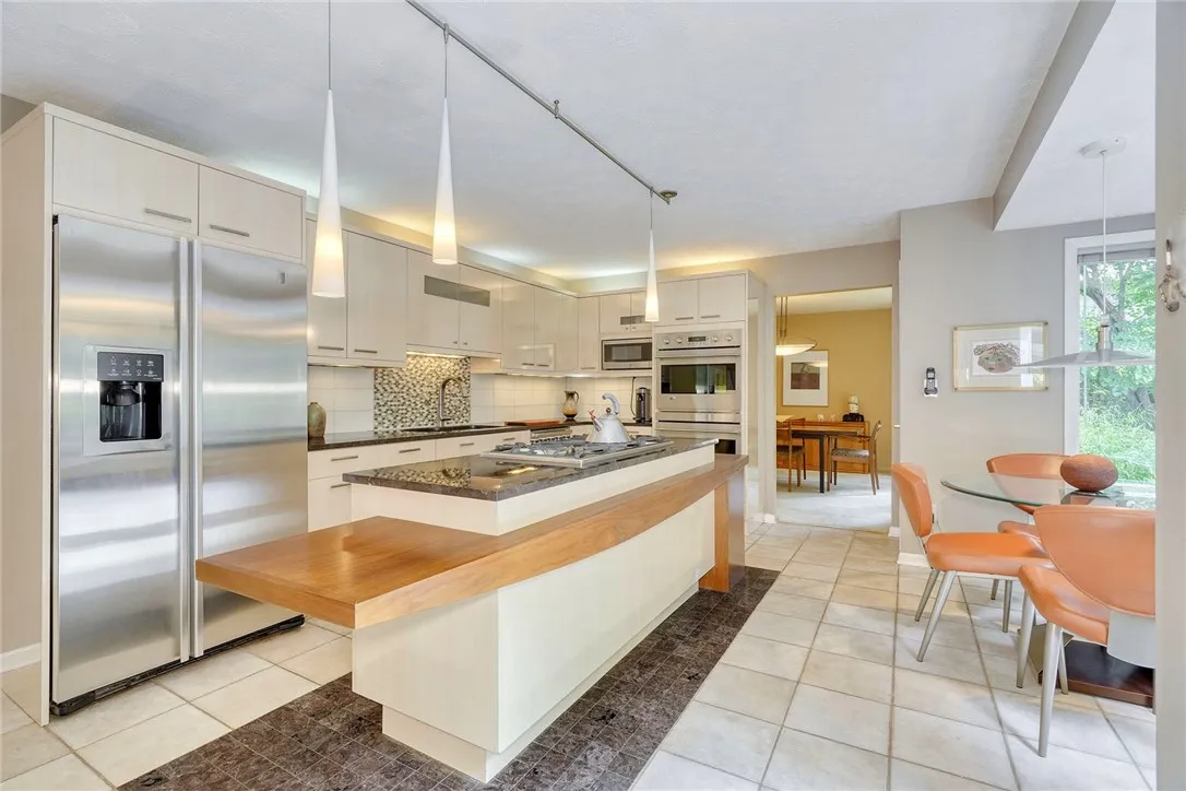 UPDATED DESIGNER KITCHEN with statement island, gas cooktop, granite counters, tile backsplash, quality cabinetry, and bright eat-in nook overlooking backyard.