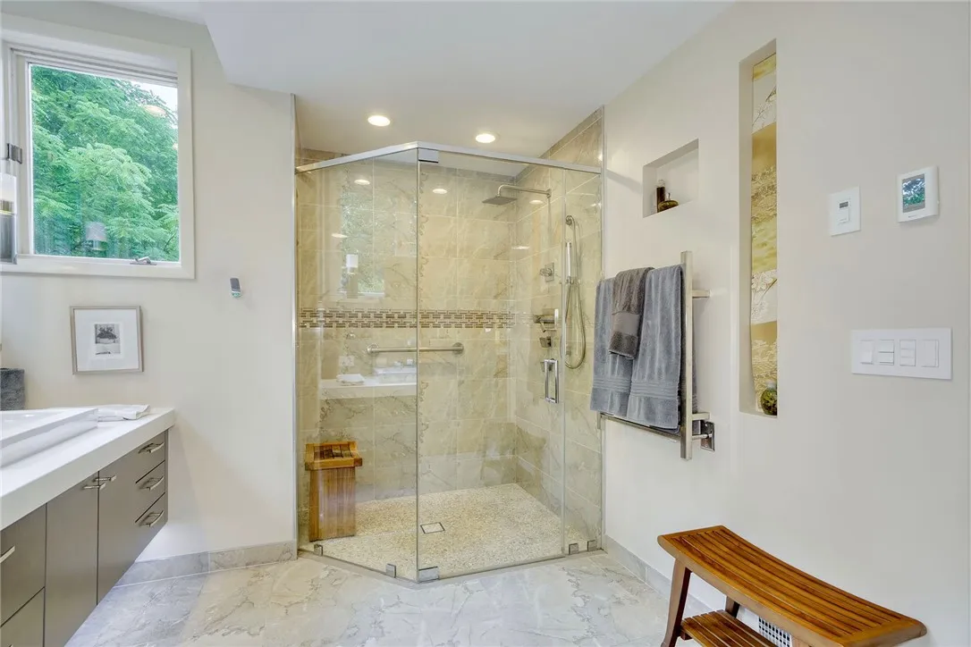 Remodeled Spa-Like en suite with heated porcelain tile, floating double vanity with underlighting, curbless shower, rainfall head + body jets. Windows wrap the vanity, bringing in natural light + treetop views